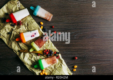 Appartamento vista laici del sacco di casa fatta frigo frullato congelati succhi yogurt gelato con frutti di bosco sul buio drammatico sfondo di legno. Snack sani c Foto Stock