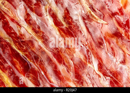 Stuzzicanti fette di prosciutto iberico in primo piano come una texture. La carne cruda che diventa un articolo di alta cucina gastronomica e di lusso, attraverso una proc Foto Stock