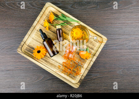 Calendula officinalis, la calendula, sinopie, comune calendula o Scotch calendula diversi prodotti di salute sul vassoio in legno, olio essenziale, tintura Foto Stock