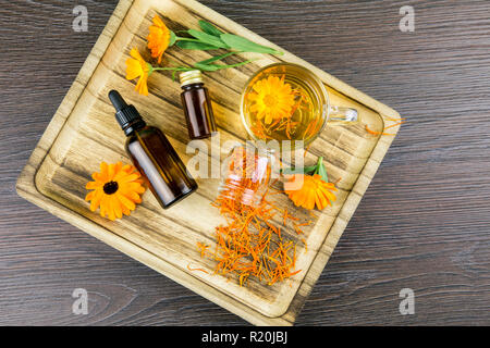 Calendula officinalis, la calendula, sinopie, comune calendula o Scotch calendula diversi prodotti di salute sul vassoio in legno, olio essenziale, tintura Foto Stock