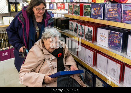 Una signora anziana in una sedia a rotelle per lo shopping Carte di Natale con il suo accompagnatore o assistente. Foto Stock