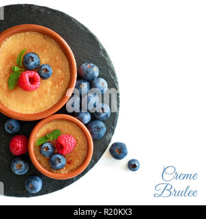 Creme brulee (crema brulee, crema bruciata) con mirtillo e lampone su pietra nera piastra isolata su bianco, copy-spazio Foto Stock