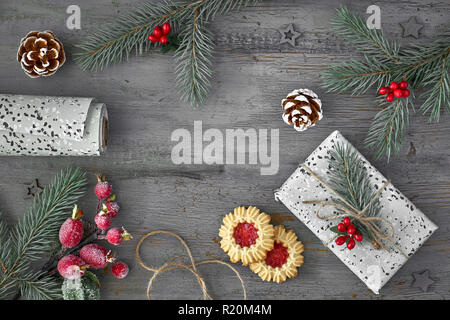 Sfondo di Natale decorato con ramoscelli di abete, marmellata cookie, avvolto dono e carta da imballaggio in legno rustico sfondo, vista dall'alto Foto Stock