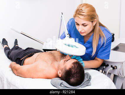 Fiducioso sorridente donna gentile cosmetologo esaminando maschio faccia del client prima di applicare la procedura in Clinica estetica Foto Stock