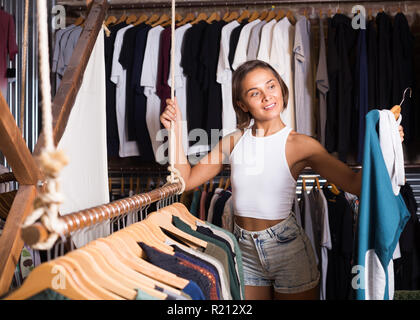 Ritratto di sorridente donna svizzera scegliendo clothers nel moderno shop Foto Stock