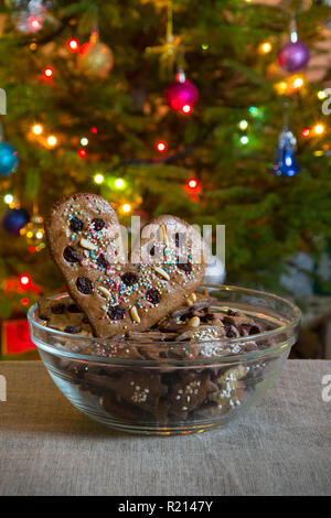 Cuore di panpepato, mettere nel recipiente di vetro. Cuore di panpepato decorate e i dolci di Natale sullo sfondo di albero di Natale decorato. Foto Stock