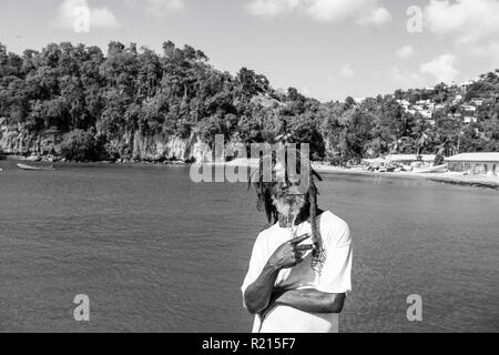 Castries, st.Lucia - 26 Novembre 2015: uomo africani mostrano la vittoria o gesto di pace sul mare blu. Il vecchio uomo senza tetto con la barba e capelli dreadlocks di sunny outdoor. La vacanza estiva, di viaggio e di wanderlust Foto Stock