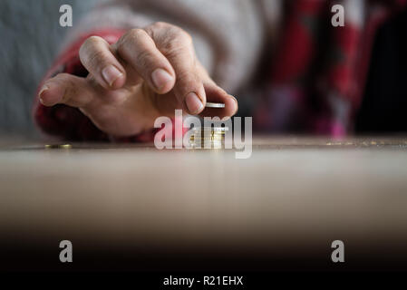 La mano della persona con le dita sporche di mettere moneta sul palo con tavola in primo piano e copia dello spazio. Foto Stock