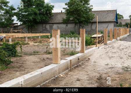 Fondazione in cemento per recinzione. Produzione di calcestruzzo di base per una staccionata di legno. Foto Stock