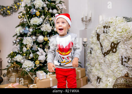 Felice famiglia giovane, padre, madre e figlio, nella sera di Natale in casa. Un ragazzino in Santa cappello del supporto vicino alla struttura con doni, stupore e ridere Foto Stock