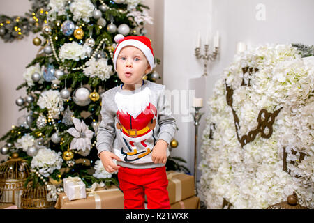 Felice famiglia giovane, padre, madre e figlio, nella sera di Natale in casa. Un ragazzino in Santa cappello del supporto vicino alla struttura con doni, stupore e ridere Foto Stock