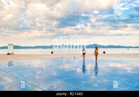 Due ragazze camminando sulla sommità del Sun Salutation installazione composta di celle fotovoltaiche vicino la riva del mare sullo sfondo di una collina e gamma Foto Stock