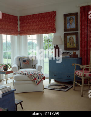 Poltrona bianca di fronte a finestre con persiane rosse Foto Stock