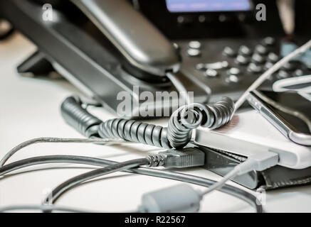 Twisted telefono cavo a spirale e altri dispositivi collegati in un ufficio Foto Stock