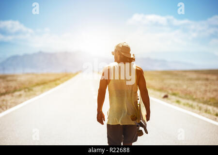 L'uomo cammina dal lungo rettilineo di autostrada o di strada con lo skateboard longboard o. Concetto di viaggio Foto Stock