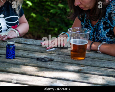 Due donne preparano una linea di cocaina su un tavolo di legno con un bicchiere di birra sul lato Foto Stock