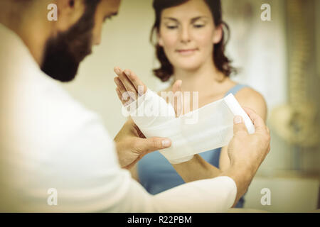 Fisioterapista mettendo fasciatura al ferito alla mano del paziente Foto Stock