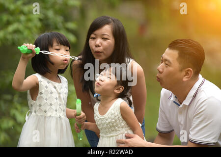 Felice giovane famiglia asiatica giocando con bacchette di bolla con la figlia nel parco all'aperto Foto Stock