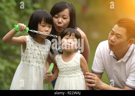 Felice giovane famiglia asiatica giocando con bacchette di bolla con la figlia nel parco all'aperto Foto Stock