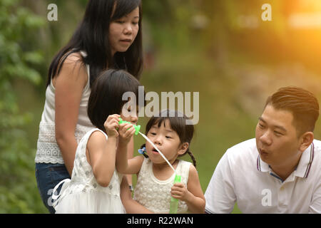 Felice giovane famiglia asiatica giocando con bacchette di bolla con la figlia nel parco all'aperto Foto Stock