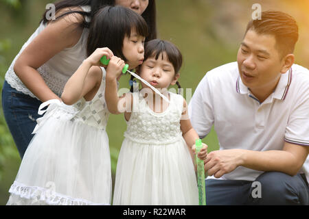 Felice giovane famiglia asiatica giocando con bacchette di bolla con la figlia nel parco all'aperto Foto Stock