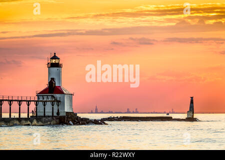 Il sole di setting back illumina il faro luminoso a Michigan City, Indiana con un raro superior mirage vision sullo skyline di Chicago all'orizzonte Foto Stock