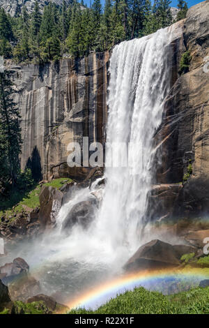 Il bagnato, misty spray primaverile circostante scende, sul fiume Merced in California il Parco Nazionale di Yosemite, rende arcobaleni colorati su una somma di estate Foto Stock