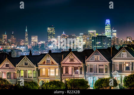 Sostenuto dalla notte skyline della città di San Francisco, in California, l'era vittoriana case vicino Alamo Square Park, sono dipinte in colori di accento Foto Stock