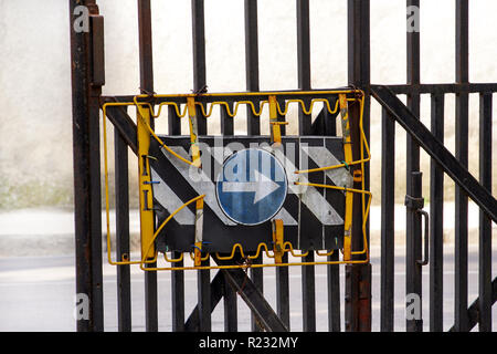 Segno di traffico in un modo strada segno con la protezione della recinzione di sicurezza / recinzione metallica con segno di traffico freccia blu / cartello blu con una freccia bianca a destra. Foto Stock