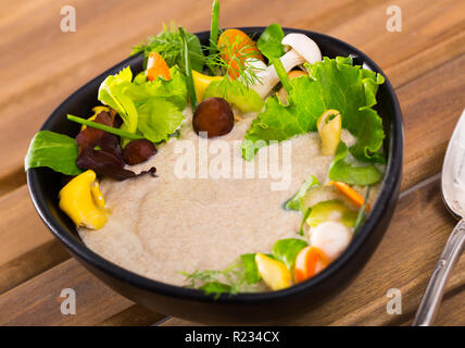 Zuppa deliziosa purea con funghi selvatici guarnito con verdure ed erbe aromatiche Foto Stock