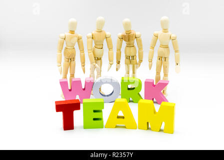 Figure in legno che si presentano come uomini di affari dietro le parole di team e lavoro, isolato su bianco. Team, unità e concetto di collaborazione Foto Stock