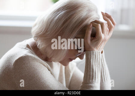 Stanco donna anziana soffre di gravi mal di testa seduto con gli occhi chiusi, esaurito femmina senior malessere aventi un forte dolore o sensazione di vertigine, sconvolto un Foto Stock