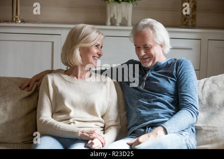 Felice di età giovane seduto sul divano accogliente a casa di parlare o di una conversazione, senior il marito e la moglie godere il tempo libero relax sul divano insieme, SMIL Foto Stock