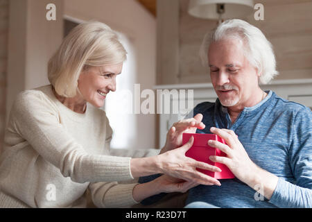 Sorridente anziana sposa rendendo sorpresa di compleanno per amato marito, uomo più anziano ottenere presente dal coniuge amorevole in occasione speciale cura coppia senior e Foto Stock