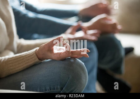 Close up di età compresa tra marito e moglie rilassarvi sul lettino meditare nella posizione del loto, senior giovane seduto sul divano a praticare yoga con mudra mani, uomo anziano un Foto Stock
