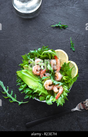 Avocado insalata di gamberetti in pietra nera di sfondo, copia dello spazio. Dieta sana insalata verde con gamberi, avocado e foglie di rucola. Foto Stock