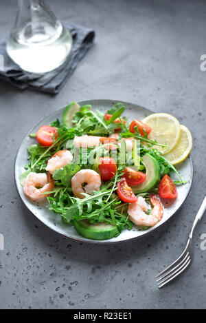 Avocado insalata di gamberetti con rucola e pomodori in pietra grigia sfondo, vicino. Dieta sana insalata verde con gamberi, avocado, cherry tom Foto Stock