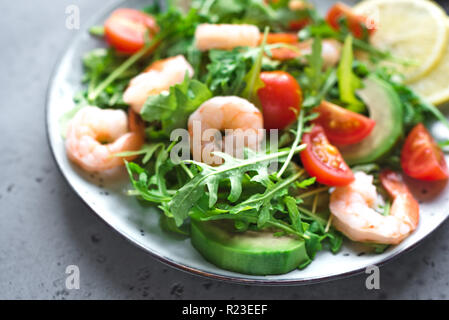 Avocado insalata di gamberetti con rucola e pomodori in pietra grigia sfondo, vicino. Dieta sana insalata verde con gamberi, avocado, cherry tom Foto Stock