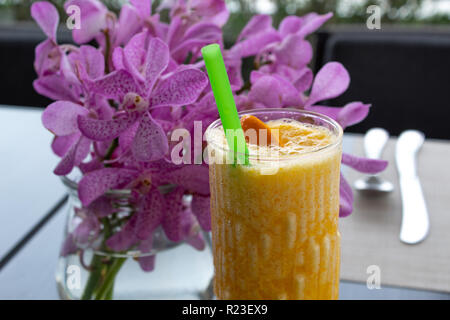 Il succo d'arancia fresco nella parte anteriore del vaso di fiori con orchidee Foto Stock