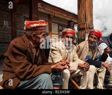 India, Himachal Pradesh, Old Manali, 08/12/2010: tre uomini anziani sedersi a parlare e fumare sotto il portico di una casa Foto Stock