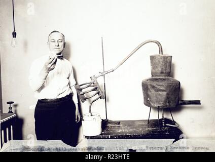 Moonshine ancora recentemente confiscati dall'Internal Revenue Bureau fotografato presso il Dipartimento del Tesoro. Uomo in piedi accanto a ancora guardando il contenuto del bicchiere. 1921 Foto Stock