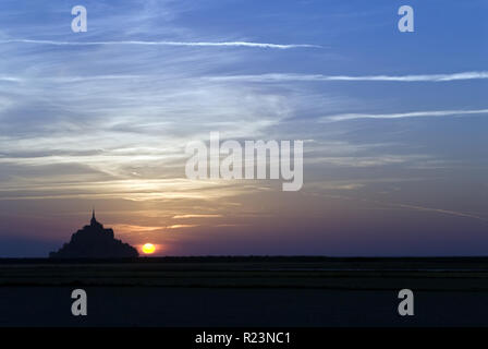 Sole che tramonta dietro al Mont-Saint-Michel (Le Mont Saint Michel), un'isola comune in Normandia, Francia noto per il suo monastero e fortificazioni. Foto Stock