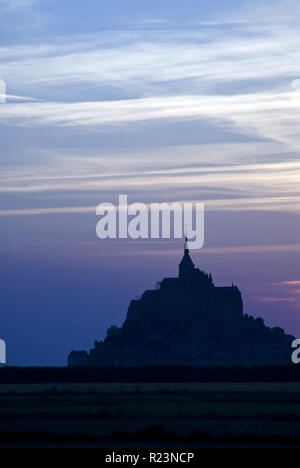 Sole che tramonta dietro al Mont-Saint-Michel (Le Mont Saint Michel), un'isola comune in Normandia, Francia noto per il suo monastero e fortificazioni. Foto Stock