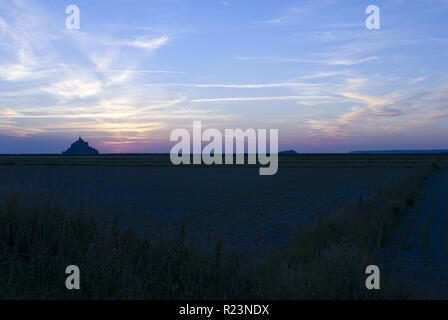 Sole che tramonta dietro al Mont-Saint-Michel (Le Mont Saint Michel), un'isola comune in Normandia, Francia noto per il suo monastero e fortificazioni. Foto Stock