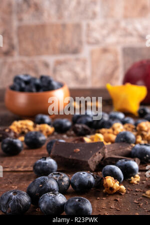 Mirtilli freschi su una tavola di legno con granola e cioccolato fondente Foto Stock