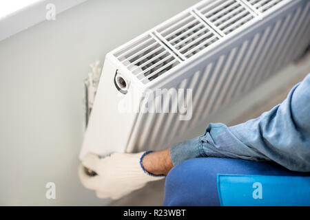 Workman acqua di fissaggio radiatore di riscaldamento sul muro bianco in interni, vista da vicino Foto Stock