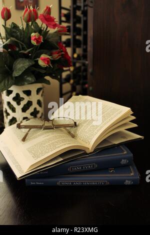 Libro aperto con gli occhiali e vaso di rose rosa Foto Stock