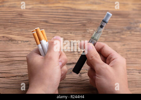 Close-up di una mano di un uomo Azienda Vape e sigaretta su sfondo di legno Foto Stock