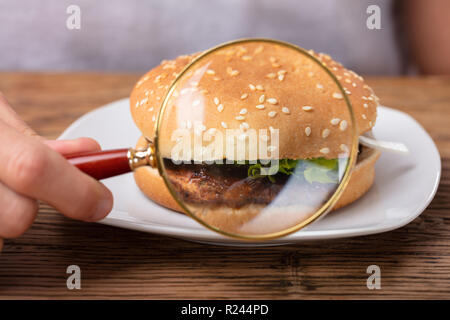 L'uomo la mano che tiene la lente di ingrandimento che mostra hamburger freschi Foto Stock