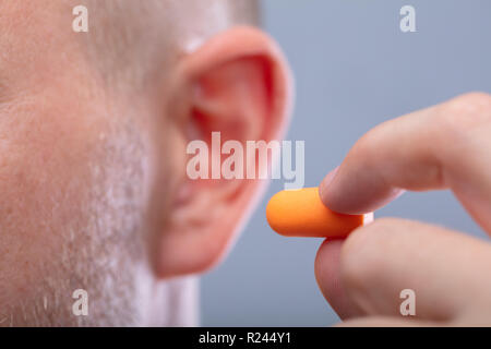 Close-up di una mano di un uomo inserimento tappo auricolare nel suo orecchio Foto Stock